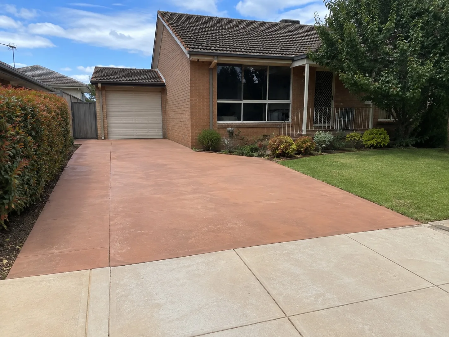 Terracotta coloured concrete driveway sweeping up to a brick Melbourne home