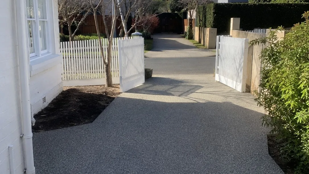 Resurfaced charcoal driveway between white fencing at a period Melbourne home