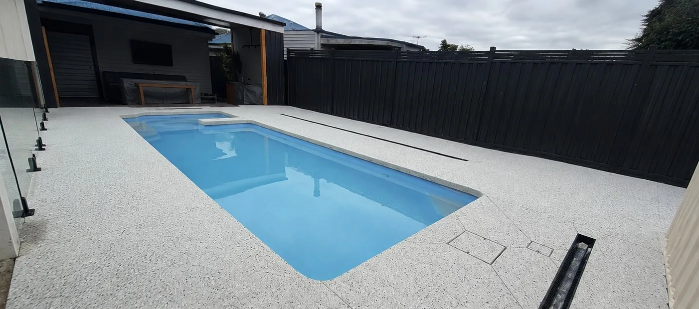White exposed aggregate pool surround with glass fencing at a Melbourne home