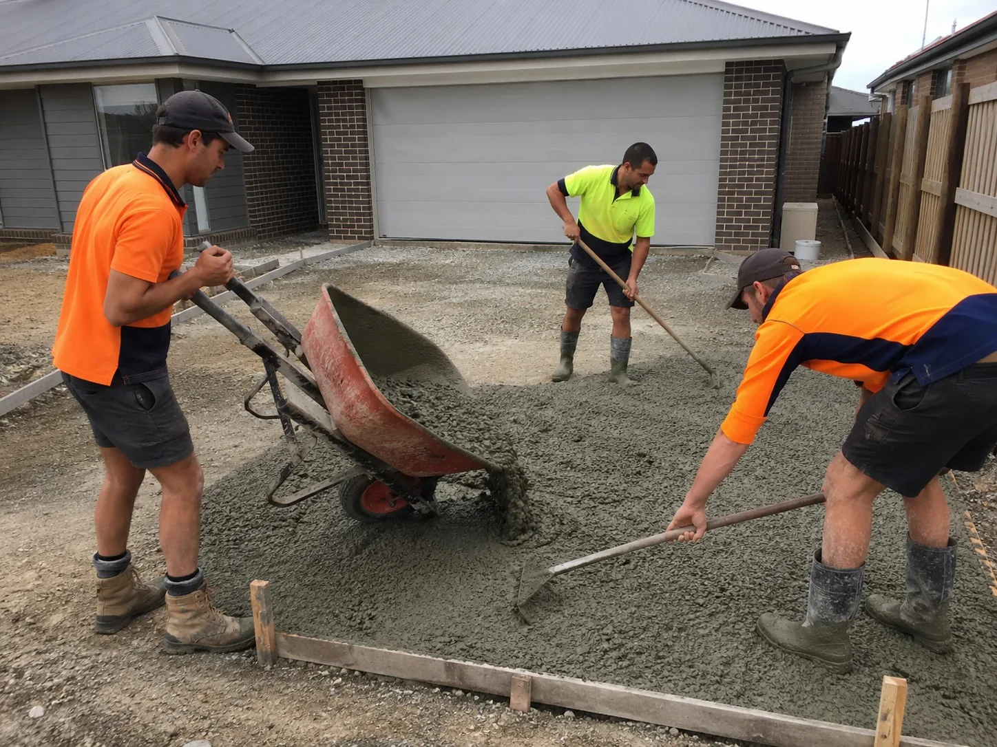 Three Melbourne concreters barrowing and raking fresh concrete into a driveway pour