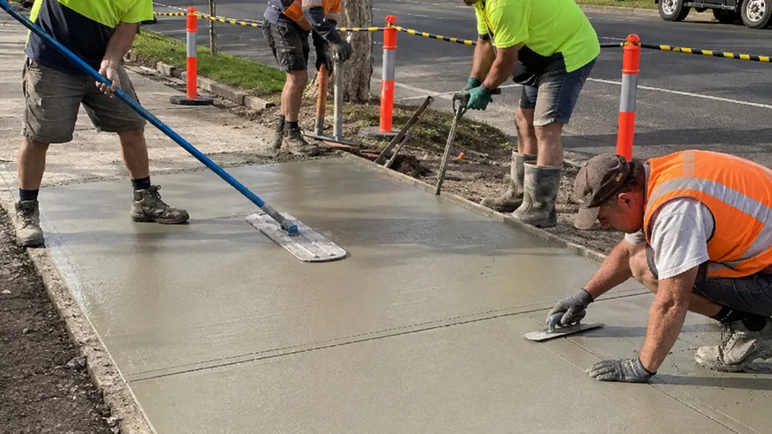 Crew screeding and finishing a replacement concrete driveway behind safety cones
