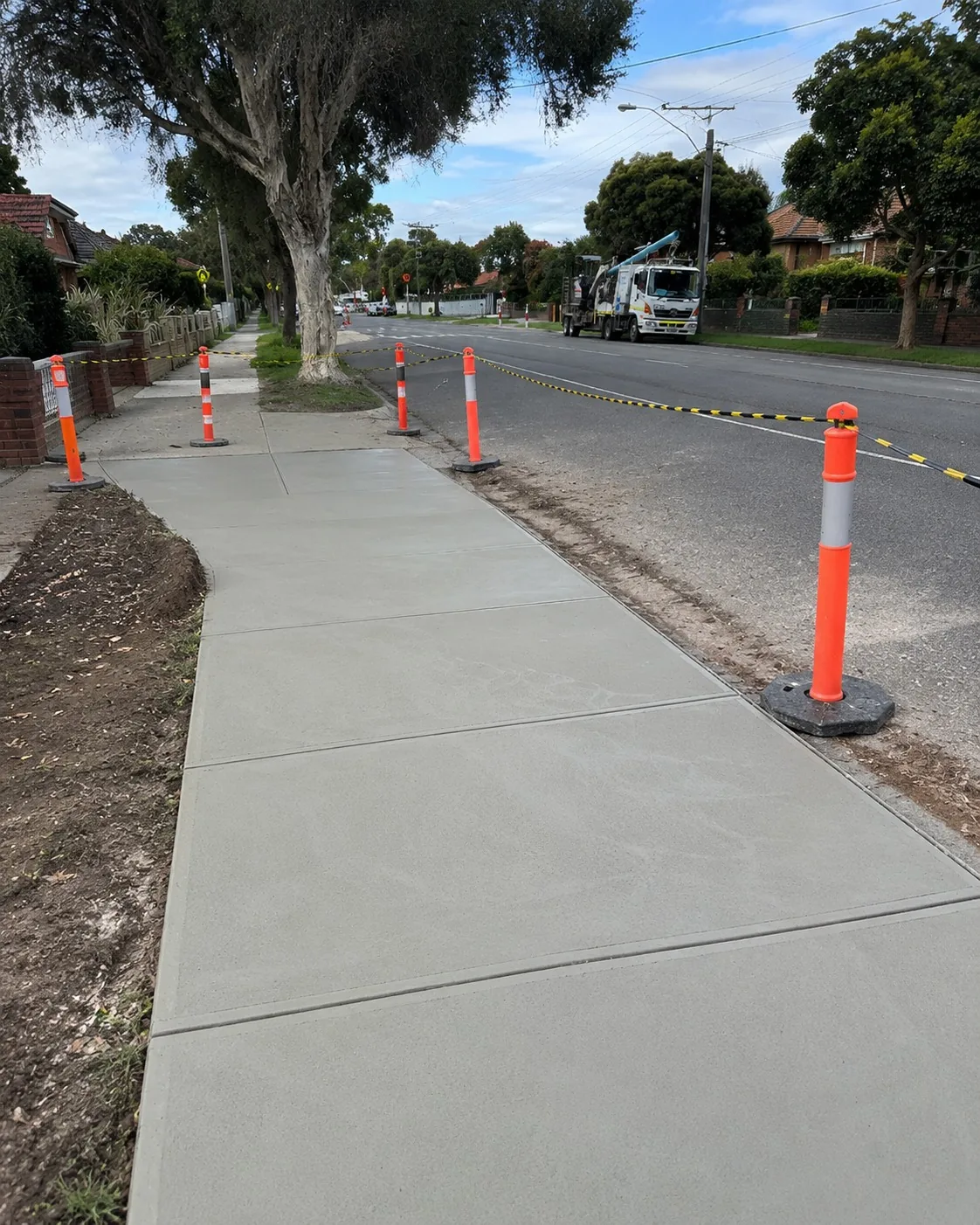 New concrete footpath running along a tree-lined Melbourne street behind bollards